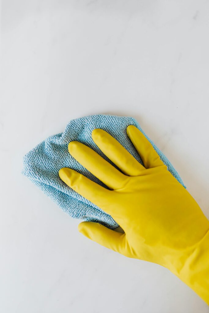 pexels-photo-4239035-4239035 Yellow gloved hand wiping surface with blue cloth, concept of cleaning and hygiene.