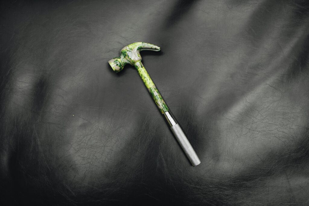 pexels-photo-5583139-5583139 Unique hammer with a colorful handle on textured black leather surface.
