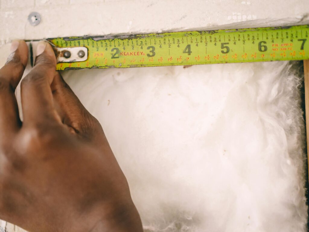 pexels-photo-8488033-8488033 Close-up of a hand measuring insulation with a yellow tape measure.